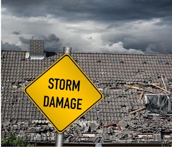 “a yellow storm damage sign in front of a large damaged roof
