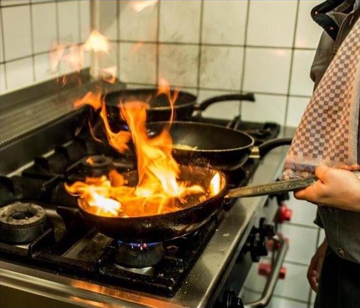 Image of a person cooking with a frying pan on fire. 