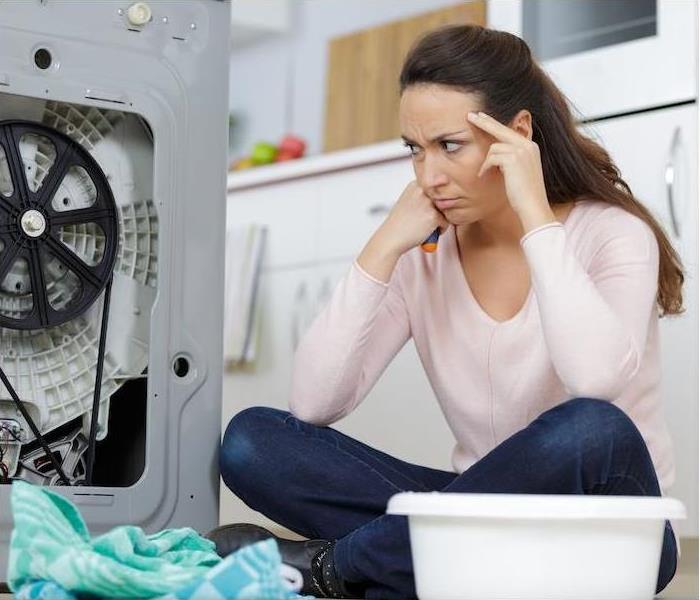 frustrated woman on floor looking at broken washer 